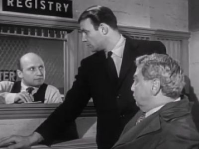 James Tolkan is sitting behind the counter as he is talking to two people.